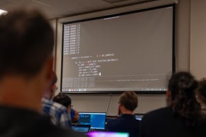 A classroom environment showing a large terminal on a projected screen with what looks like python code.